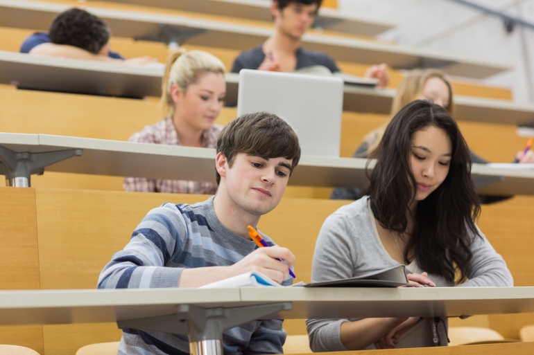 Students listening and taking notes in a lecture hall in college